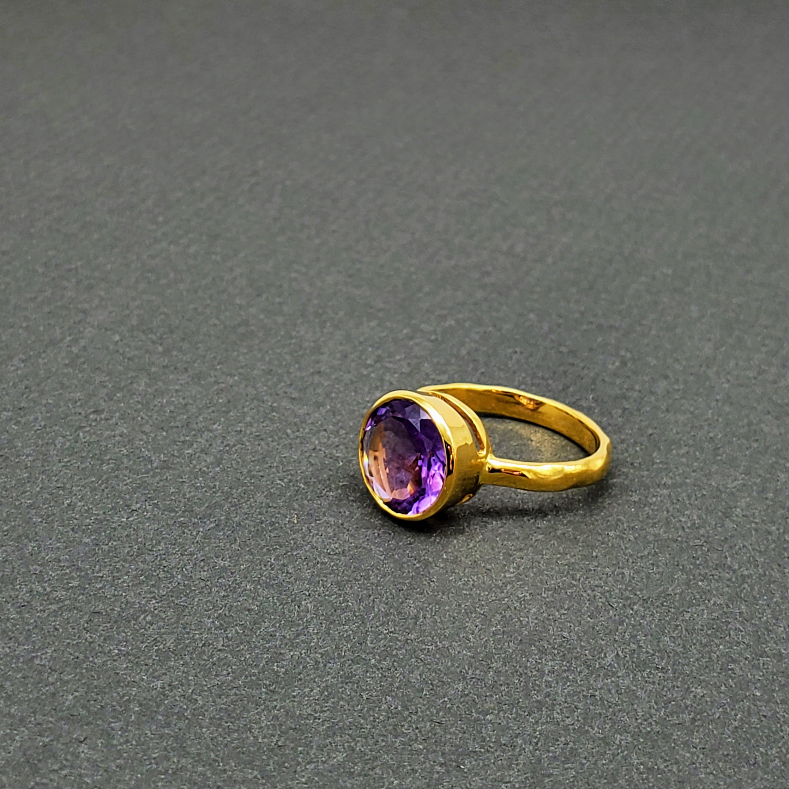 Vibrant round-cut Amethyst Center stone encased in 14k gold and a pounded band. The texture of the band brings in light to enhance the beauty of the stone
14 Kt Yellow Gold
Amethyst
Hand Crafted
available in every size
Round cut