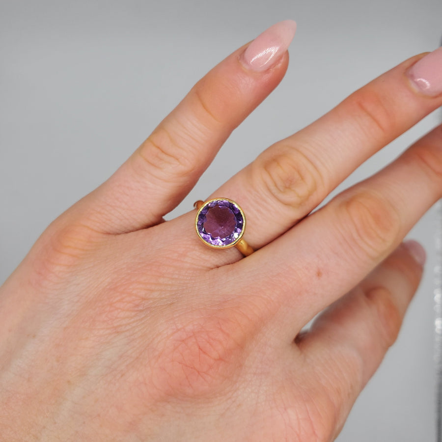 Vibrant round-cut Amethyst Center stone encased in 14k gold and a pounded band. The texture of the band brings in light to enhance the beauty of the stone
14 Kt Yellow Gold
Amethyst
Hand Crafted
available in every size
Round cut