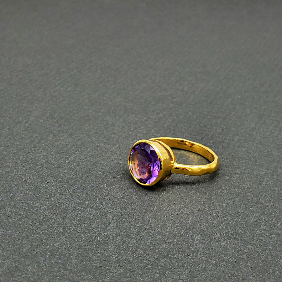 Vibrant round-cut Amethyst Center stone encased in 14k gold and a pounded band. The texture of the band brings in light to enhance the beauty of the stone
14 Kt Yellow Gold
Amethyst
Hand Crafted
available in every size
Round cut